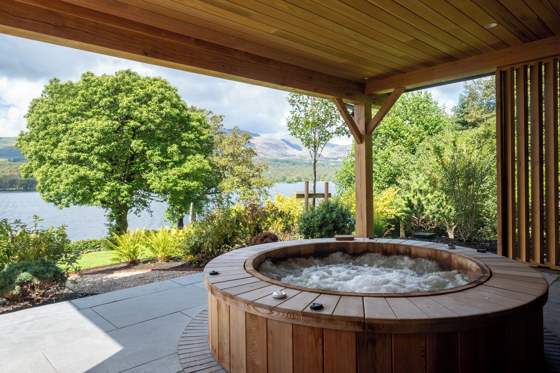 A wooden hot tub with a view of a lake and mountains.