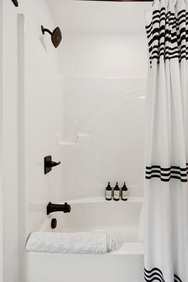 Une salle de bain moderne équipée d’une baignoire, d’une douche, d’un porte-serviettes et d’un ensemble de produits de toilette.