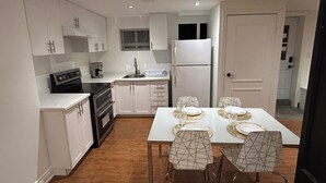 Cozinha compacta com armários brancos, forno embutido e geladeira. Há uma mesa de jantar com quatro cadeiras e toalha de mesa branca.