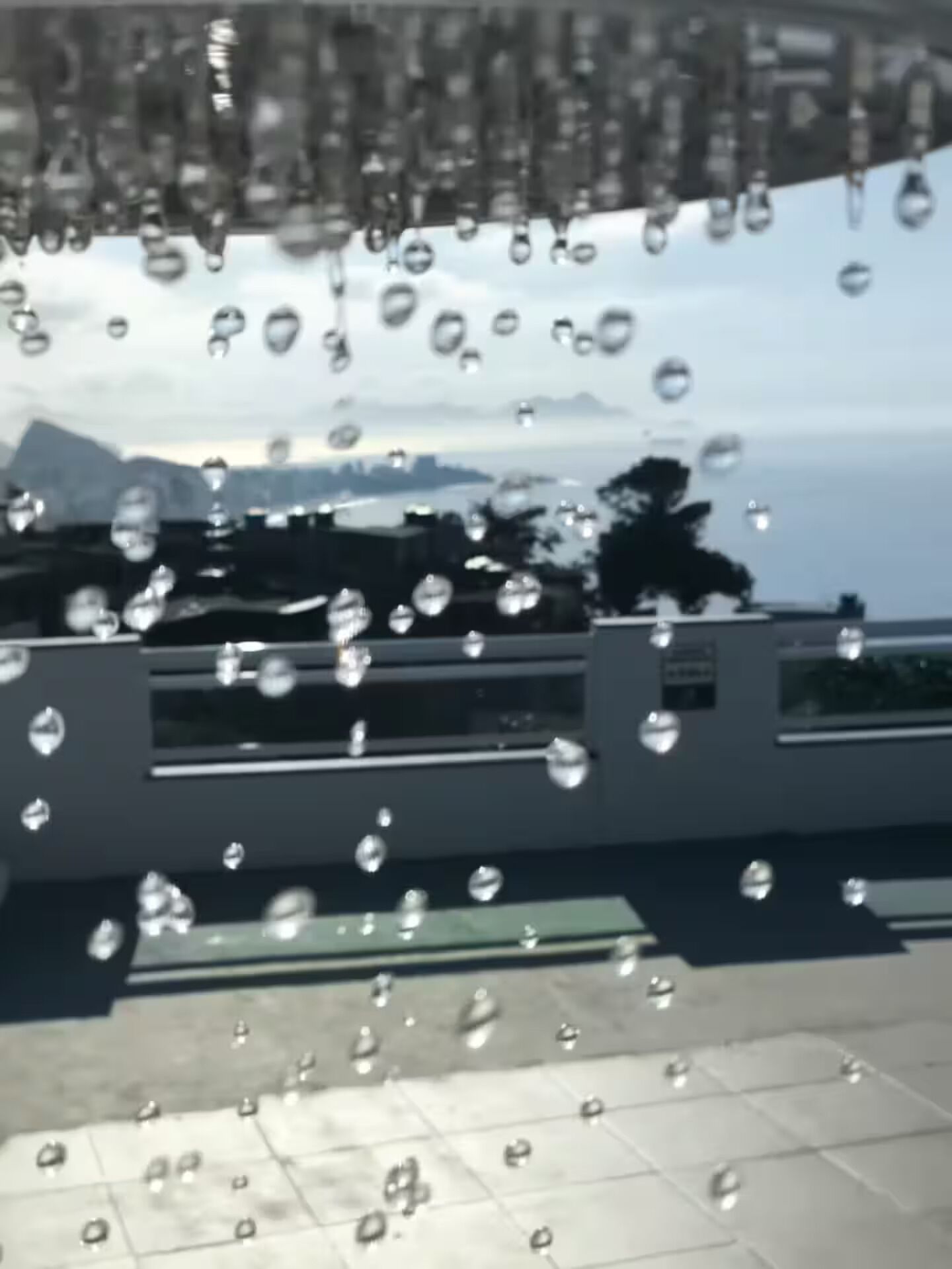 A view through a window with raindrops, a railing, and a distant landscape.