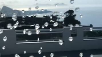 A view through a window with raindrops, a railing, and a distant landscape.