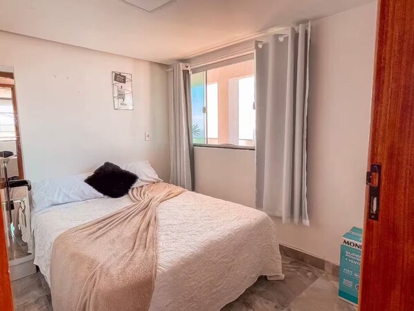 A bedroom with a bed, a window with curtains, a door, and a sign on the wall.