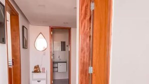 Un pasillo con piso de mármol, una consola blanca con espejo y una puerta de madera.
