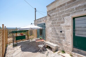 A stone building with a green door, a small table with a chair, and a white umbrella.