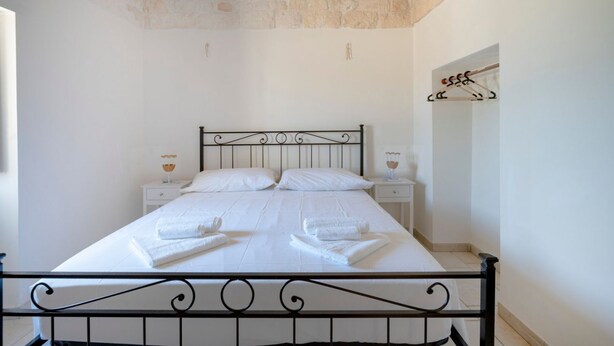 Una cama bien hecha con sábanas y toallas blancas, techo de piedra y una sencilla mesita de noche con lámpara.