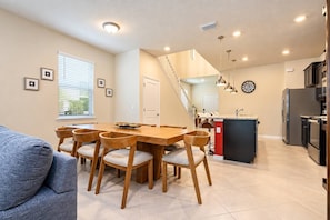 A modern kitchen with a dining area, a staircase, and a living room with a sofa.
