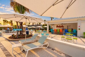 Un espace aménagé au bord de la piscine, avec des chaises longues, des parasols et un coin bar doté de chaises aux couleurs vives.