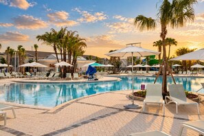 Une piscine entourée de palmiers, avec des chaises longues et des parasols.