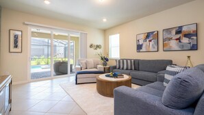A modern living room with a grey sofa, a round coffee table, and a beige couch. There are two abstract paintings on the wall and a vase with flowers on a side table. - Super Modern 7BR Windsor Cay* (Clermont)