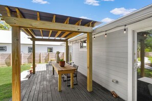 Een houten terras met een pergola, een tafel met stoelen en een plant in pot.