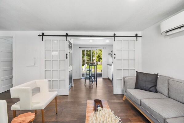 Een moderne woonkamer met een witte bank, een grijze bank en een witte stoel. Een houten salontafel staat in het midden.