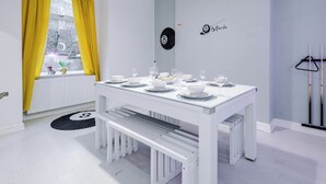A dining area with a white table set for four, a bench, and a window with yellow curtains. - Sleep 7, Pool Table/TTennis, Free Parking, 3BR (Manchester)
