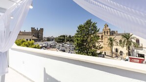 Un balcón con vista a una plaza histórica con un edificio parecido a un castillo y palmeras.