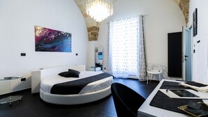 Un dormitorio moderno con una cama redonda, un escritorio con silla, un ventanal con cortinas y un diseño de techo singular.