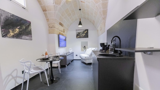 Una cocina compacta con techo abovedado de piedra, una zona de comedor con sillas blancas, un sofá y obras de arte en las paredes.