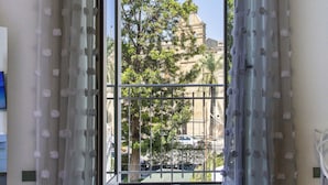 Una habitación con un ventanal grande, cortinas traslúcidas con detalles de pompones y vistas a un balcón y árboles fuera.