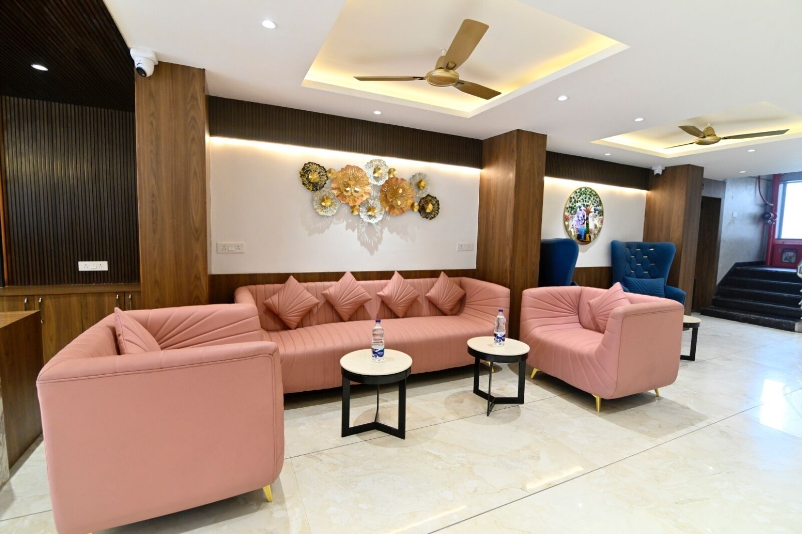 A modern lobby with a pink sofa set, two side tables, and a blue armchair.