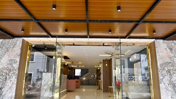 A modern hotel entrance with glass doors, a marble floor, and a ceiling with wooden panels and recessed lighting. - Carry Plus Hotel (Indore)