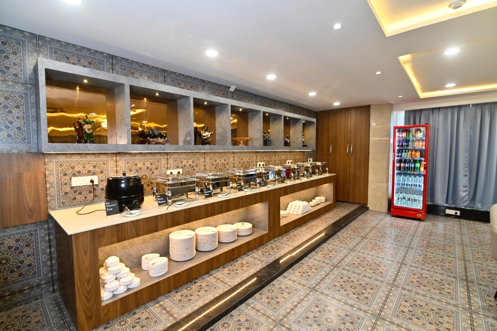 Un área de desayuno de hotel con una barra larga, máquinas de café y un dispensador de bebidas.