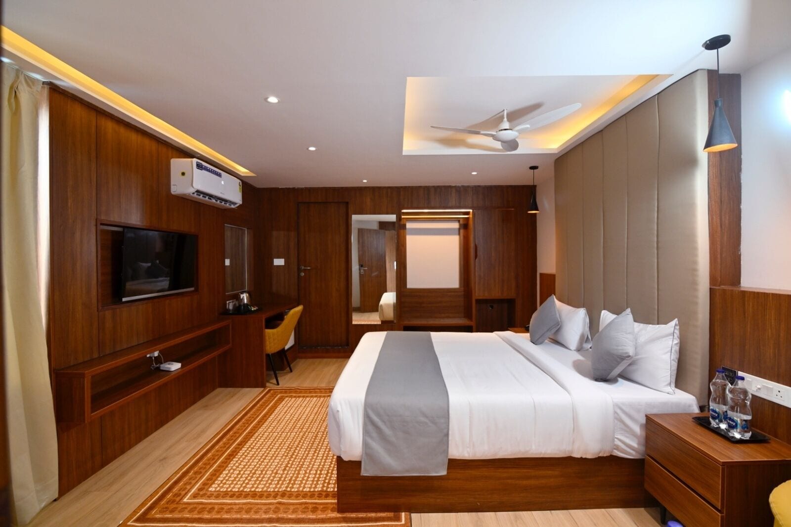 Une chambre d’hôtel moderne équipée d’un grand lit, d’un bureau avec une chaise, d’une télévision et d’un ventilateur de plafond.