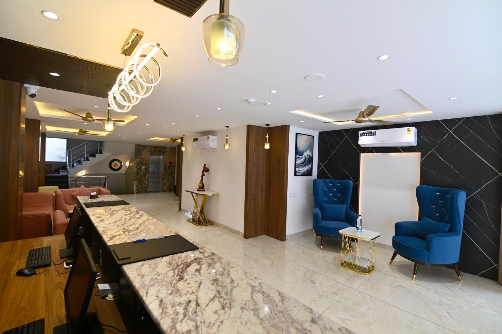 A modern hotel lobby with a marble reception desk, blue armchairs, and a staircase leading to the upper floors.