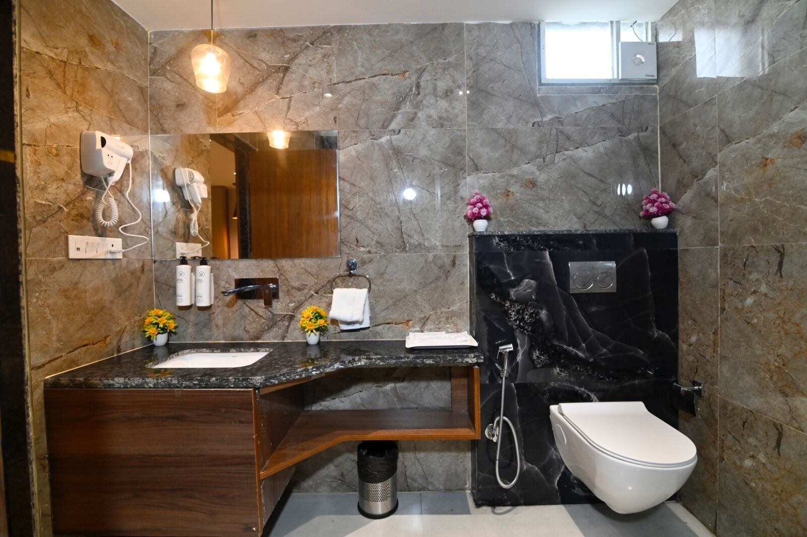 A modern bathroom with a marble wall, a wooden vanity, a white sink, a toilet, and a shower.