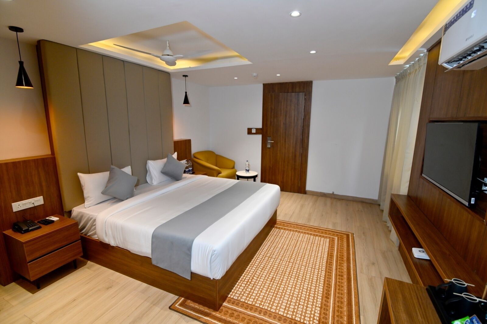 Ein modernes Hotelzimmer mit einem großen Bett, einem Holzkopfende, einem Flachbildfernseher, einem Schreibtisch und einem Sessel.