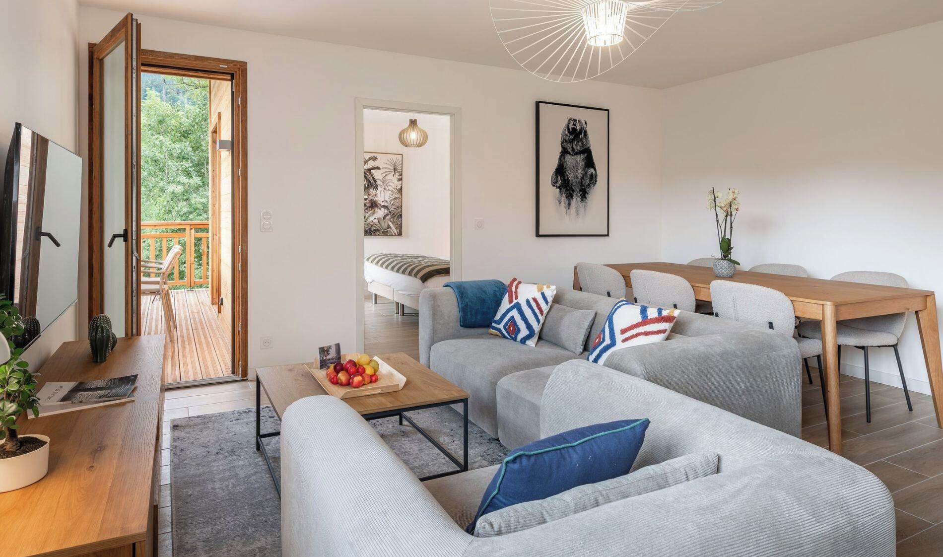 Ein modernes Wohnzimmer mit einer Sofagarnitur, einem Esstisch mit Stühlen, einem Couchtisch und einem Fernseher auf einem Holzständer.