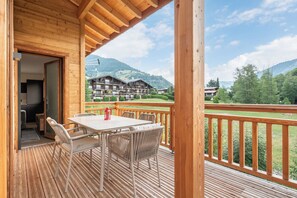 A wooden deck with a table and chairs, overlooking a mountainous landscape and a hotel building.