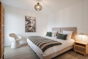 A bedroom with a large bed, a chair, a nightstand, and a wall-mounted lamp.