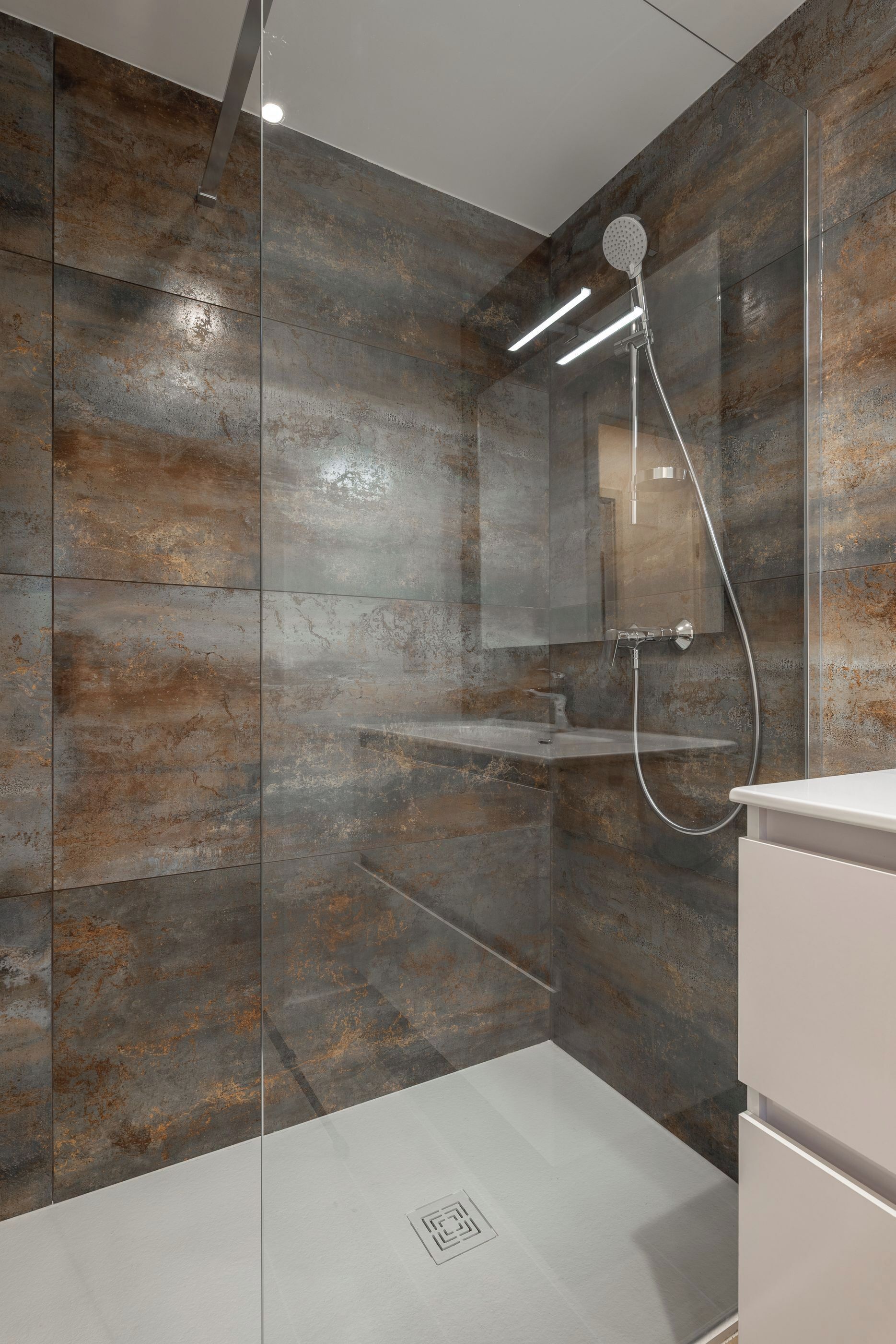 A modern shower with a glass enclosure, a built-in mirror, and a white vanity.