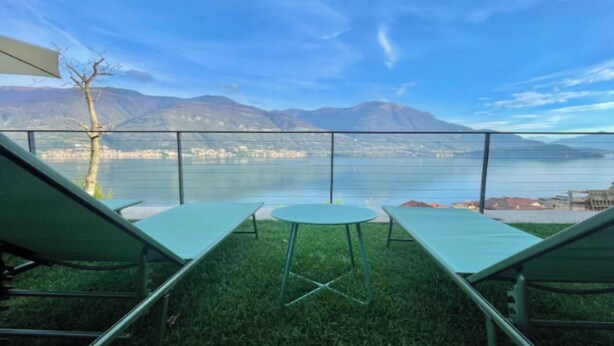 Een terras met twee groene loungestoelen en een tafeltje, met uitzicht op een meer en bergen.
