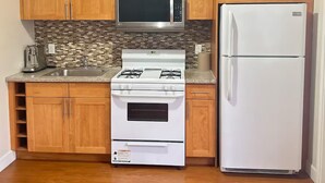 Una cucina con mobili in legno, un forno a microonde in acciaio inox, un piano cottura e un frigorifero bianchi.