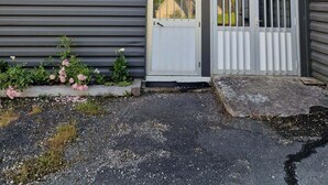 En modern byggnad i två våningar med en grå fasad, en vit dörr med ett säkerhetsgaller och ett litet fönster ovanför dörren.