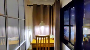 A narrow hallway with a wooden table and chairs, a hanging light fixture, and a window with a view of the street outside.