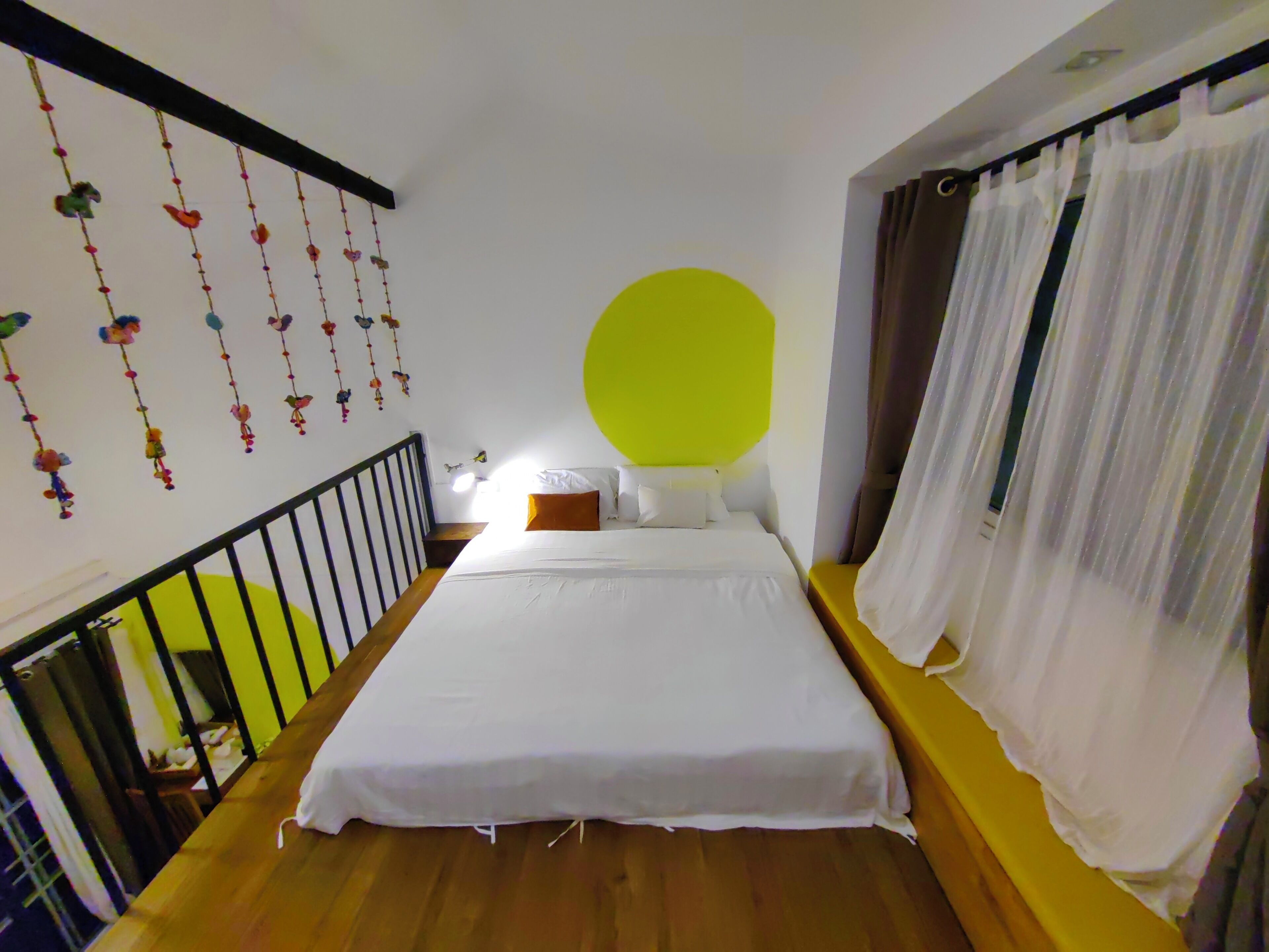 A bedroom with a bed, a window with curtains, a staircase, and wall decorations.