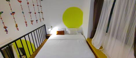 A bedroom with a bed, a window with curtains, a staircase, and wall decorations.