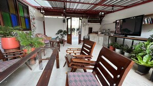 A cozy outdoor seating area with wooden furniture, a TV, and various potted plants.