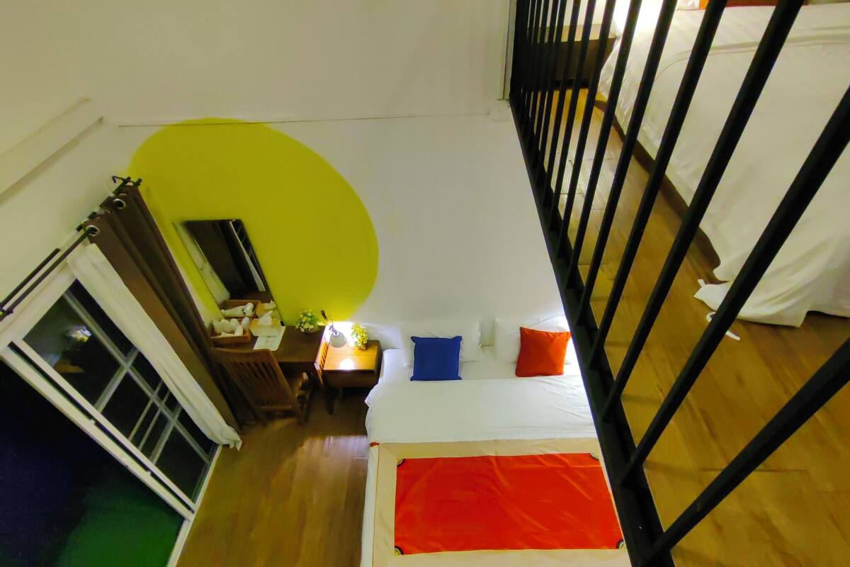 A high-ceiling room with a bed, a small table, and a window.