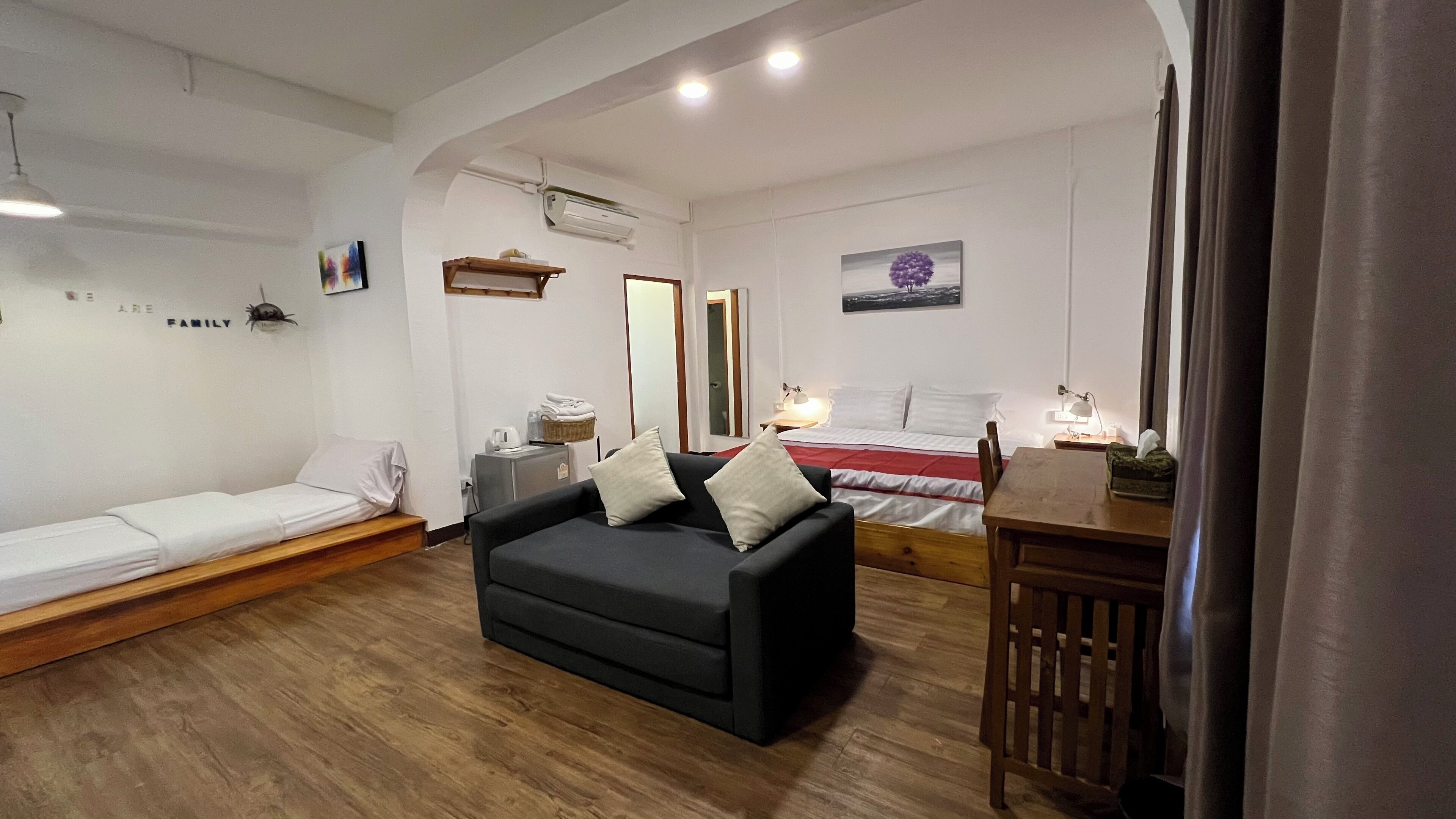 A bedroom with a bed, a sofa, a desk, and a chair. There is a mirror, a lamp, and a picture on the wall.