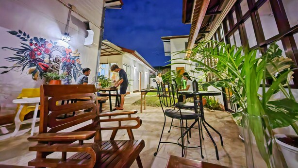An outdoor patio area with wooden benches and tables, surrounded by potted plants and a mural on the wall.