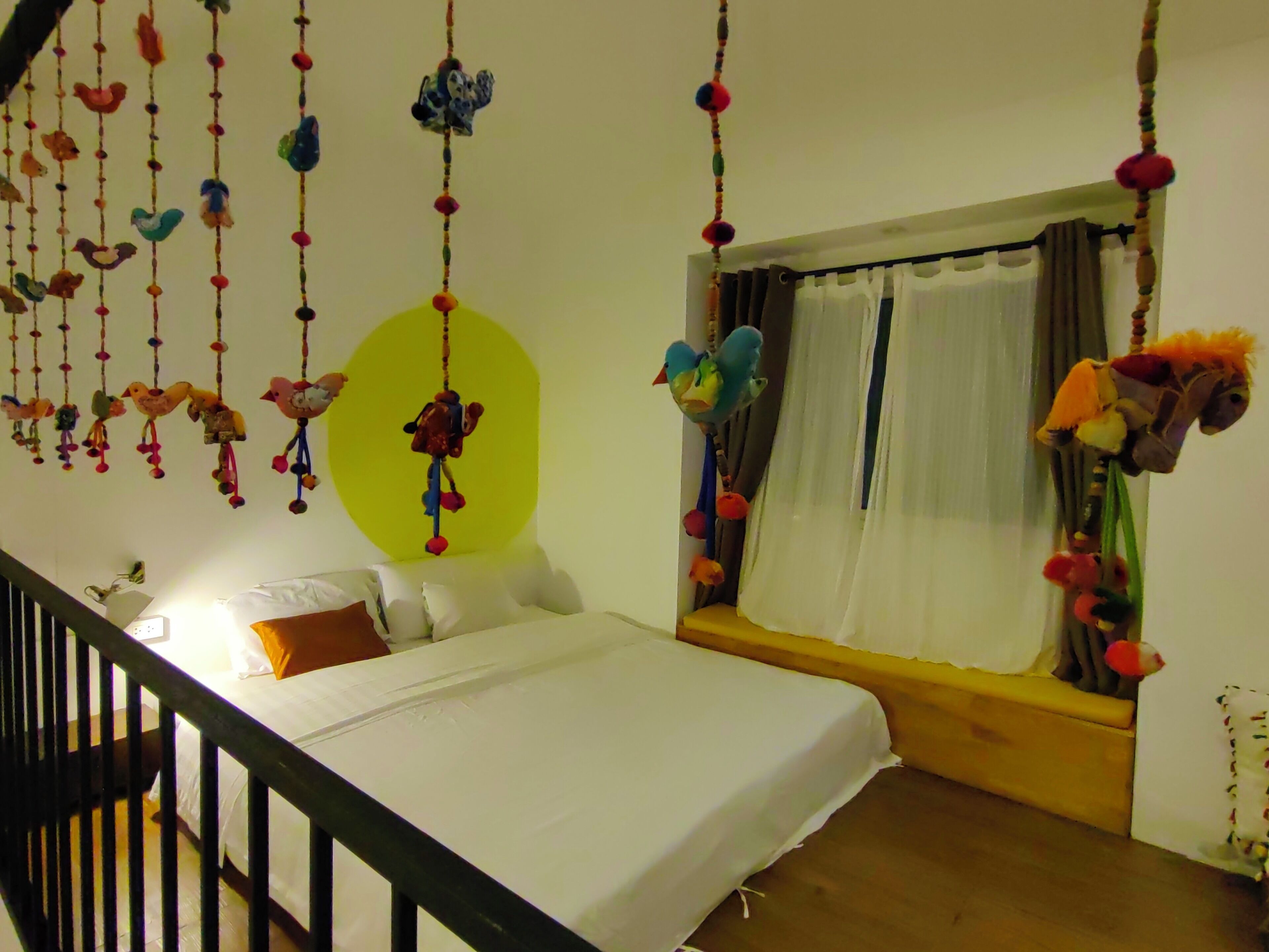 Een slaapkamer met een bed, een raam met gordijnen en een hangende vogeldecoratie.