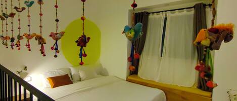 Een slaapkamer met een bed, een raam met gordijnen en een hangende vogeldecoratie.