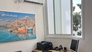 A modern office space with a desk, chair, printer, and computer monitor. A large window provides a view of a coastal town. - Office/apartment combo Rothschild Blv in TelAviv! Parking, elevator, shelter (Tel Aviv-Yafo)