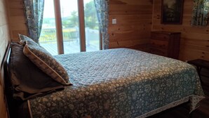 A wooden room with a bed, a dresser, and a window with curtains.