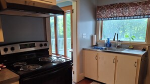 A kitchen with a black stove, white cabinets, and a window with a view of trees.