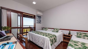 A hotel room with a bed, a desk with a laptop, a chair, a potted plant, and a view of the sea through a window. - Praia Grande Hotel (Fundão)