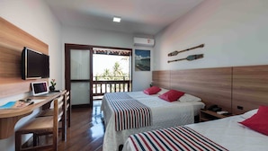A hotel room with two beds, a desk with a computer, a TV, and a balcony with a view of palm trees. - Praia Grande Hotel (Fundão)