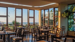 A restaurant with large windows offering a view of the beach and ocean. Tables and chairs are arranged for dining. - Praia Grande Hotel (Fundão)