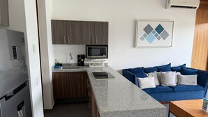 A modern kitchen with a built-in microwave, a sink, and a countertop. There is a blue sofa with cushions in the living area. - Escapada junto al mar en B Nayar (Cruz de Huanacaxtle)